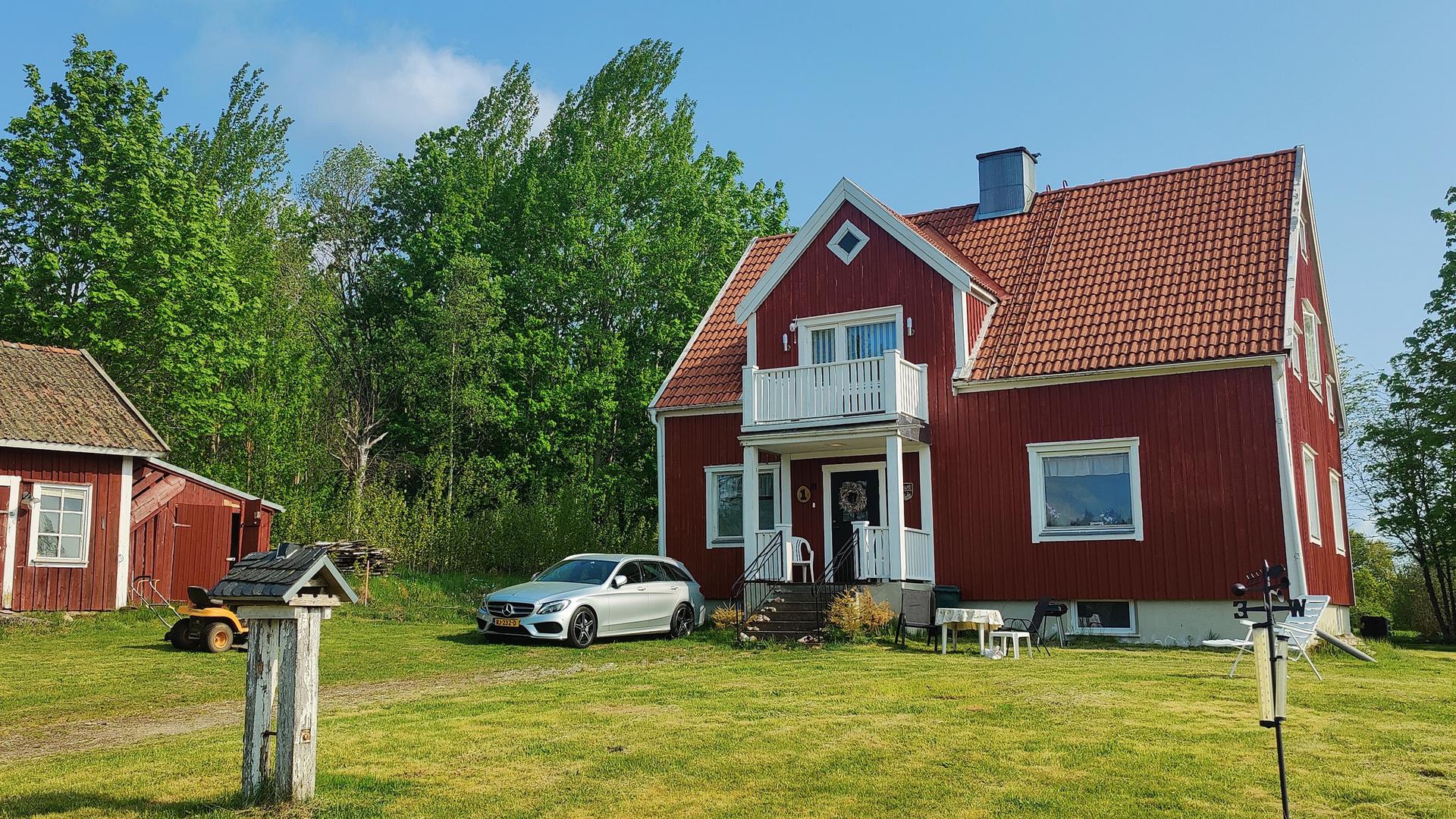 Faluröd stuga med vita knutar, veranda och balkong.